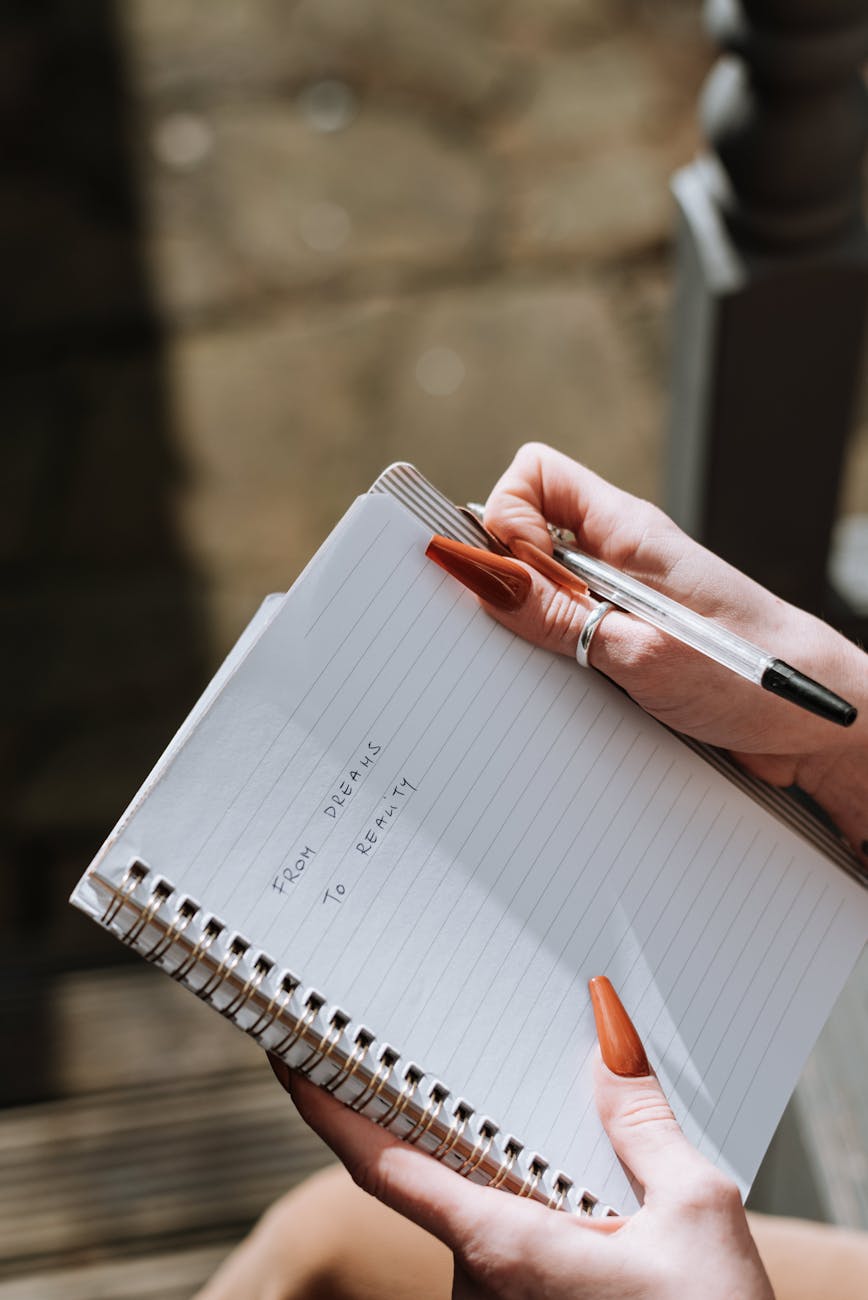 woman with long nails writing text in diary